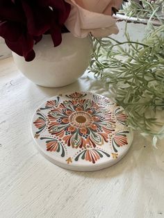 Add a touch of bohemian flair to your decor with this beautiful 3.5 inch ceramic coaster featuring a hand painted mandala pattern. Each coaster is meticulously painted by hand, making it a unique and eye-catching addition to your home. Perfect for protecting your surfaces in style, this coaster is both practical and stylish. Bring a pop of color and personality to your space with this one-of-a-kind piece. Great for gifting or treating yourself! Hand Painted Ceramic Coasters Size: 3.5 inch round, 1/4 inch thick Design: Coral & Green On White Ceramic Base Materials: ceramic, acrylic paint, sealant Please note- though a sealant was used to protect the paint, it is not recommended to submerge in water. Spot clean as needed.  Not recommended for direct contact food.  Any accessories shown sitti Painted Ceramic Coasters, Clay Coasters, Paint Sealant, Coaster Art, Painted Mandala, Diy Ceramic, Hand Making, Diy Coasters, Ceramic Base