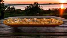 a wooden table topped with a glass bowl filled with crystal stones next to the ocean