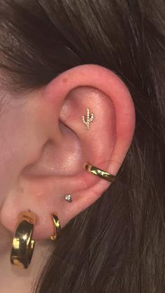 a woman wearing gold ear piercings with an arrow on the top and two small hoop earrings