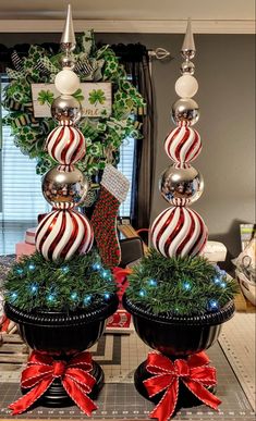 two christmas decorations on top of black pots with red and white striped balls in them