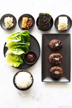 an assortment of food on black plates and white counter top with sauces, rice, lettuce, and other items