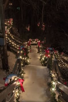 a walkway covered in christmas lights and wreaths with red bows on the top, surrounded by snow