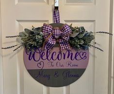 a welcome sign hanging on the front door of a house with purple and green accents