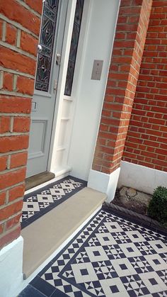 a black and white tiled floor next to a brick building with an open front door