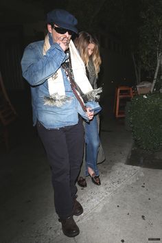 a man in a blue jean jacket and hat walking down the street with a woman