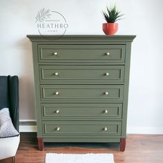 a green dresser sitting next to a black chair and potted plant on top of it