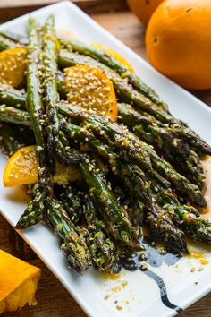 asparagus, oranges and sesame seeds on a white plate next to sliced oranges