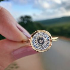 a woman's hand holding a ring with a diamond in the middle and sky behind it