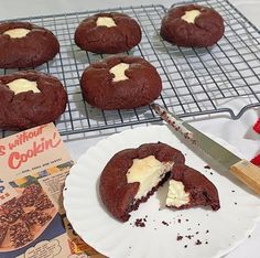 chocolate cookies with white frosting are on a cooling rack next to a book and knife