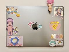 an apple laptop covered in stickers and magnets, with a doll on top