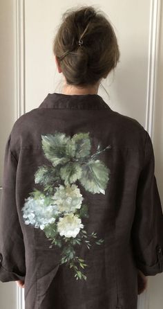 a woman standing in front of a door with her back turned to the camera, wearing a brown jacket with flowers on it