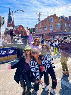 four women pose for a photo in front of a crowd on the street with their arms around each other