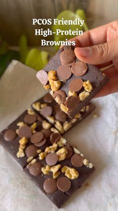 two pieces of chocolate with walnuts and peanuts on top are being held by a hand