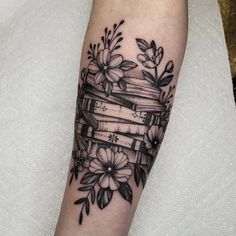 a black and white photo of a book tattoo on the left arm with flowers around it