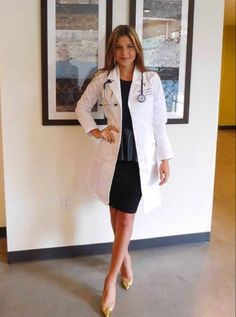 a woman standing in front of a wall wearing a white lab coat and black dress