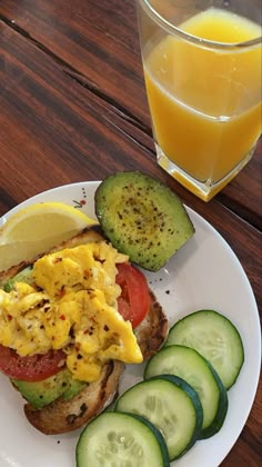 a white plate topped with a sandwich and cucumbers next to a glass of orange juice