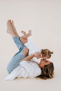 a woman holding a baby while laying on the ground with her legs up in the air