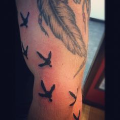 a man's arm with birds flying around it and a feather in the middle