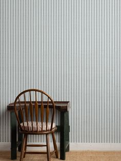 a wooden chair sitting in front of a wall with vertical stripes on it's side