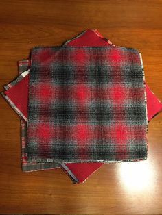 three red and black plaid napkins sitting on top of a wooden table