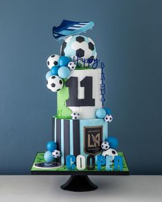 a soccer themed birthday cake on a table with blue and white balloons in the shape of a number one