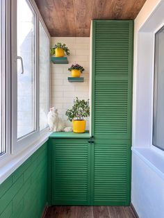 a green cabinet in the corner of a room next to a window with potted plants on it