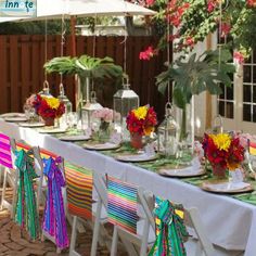 a long table set up with colorful flowers and place settings for an outdoor dinner party