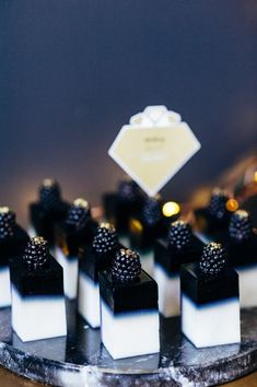 small black and white desserts are arranged on a marble platter with lights in the background