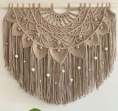 a macrame wall hanging with tassels and beads on a white wall