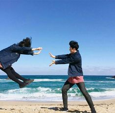 two people on the beach playing with a frisbee and another person jumping in the air