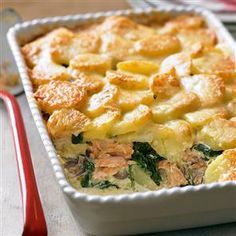 a casserole dish with potatoes and spinach on a wooden board next to glasses