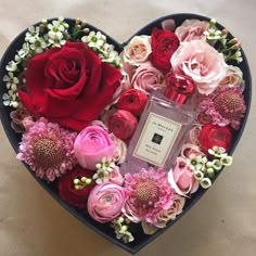 a heart shaped box filled with flowers and a bottle of perfume in it's center