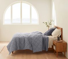 a bed with a blue quilt on it in front of an arched window and wooden floor