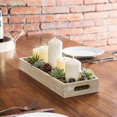 a wooden tray with candles and succulents in it sitting on a table