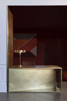 a gold table with a lamp on it in front of a wall and flooring