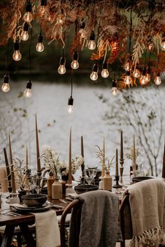 an outdoor dining table set for dinner with candles and lights hanging from the ceiling over it