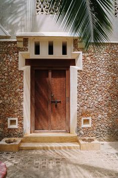 an entrance to a house with stone walls and wooden door, surrounded by palm trees