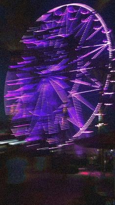 a ferris wheel lit up at night with purple lights and blurry image in the background