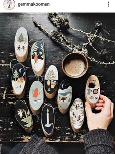 someone is holding their shoes in front of many painted shoes on a table next to a cup of coffee