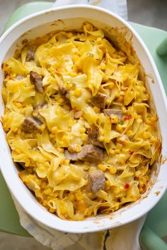 a casserole dish with meat and noodles in it on a green tablecloth