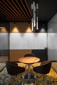 an empty meeting room with three chairs and a round table in the foreground, lights above it