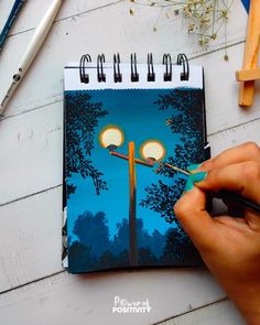 a hand is holding a pencil and drawing on a notebook with an image of a street light