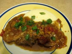 a plate topped with meat covered in gravy next to mashed potatoes and green onions