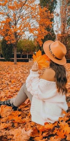 a woman sitting on the ground with leaves in her hand and wearing a cowboy hat