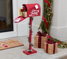 a red mailbox with presents tied to it on the front porch next to christmas decorations