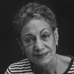 an older woman with curly hair wearing a striped shirt and necklace smiles at the camera