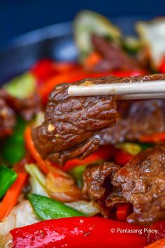 meat and vegetables being stir fried in a wok with chopsticks on top