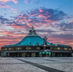 a large building sitting on top of a cobblestone street next to a sky filled with clouds