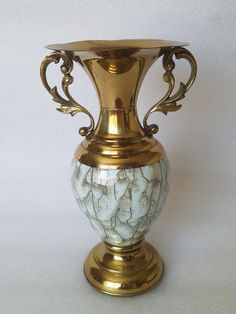 an ornate gold vase with white marble on the bottom and sides, sitting against a white background