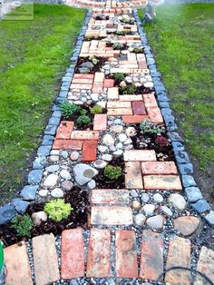 a long brick path is lined with small stones and plants in the middle of it